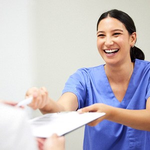 Dental assistant smiling while handing patient form