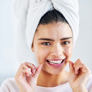 Woman smiling while flossing her teeth in bathroom