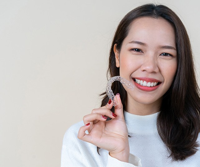 Woman smiling while holding clear aligner
