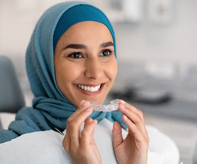  Woman smiling while holding clear aligner in treatment room