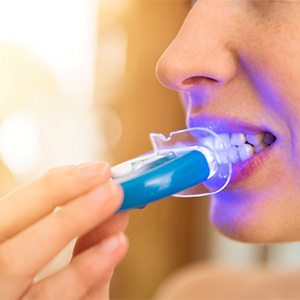 Nose-to-neck view of someone applying take-home whitening light to their teeth